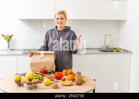 La femme règle les achats dans la cuisine. Livraison de produits d'épicerie dans des sacs en papier. Service d'abonnement de l'épicerie dans des conditions de quarantaine parce que Banque D'Images