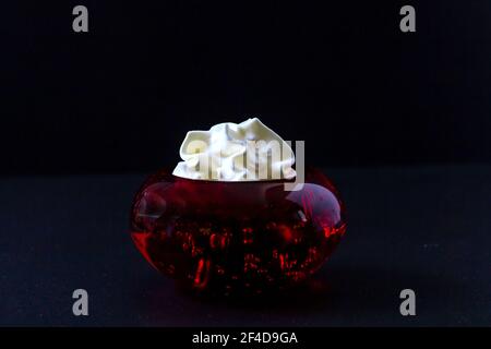 Crème fouettée à l'intérieur d'un contenant en verre rouge. Banque D'Images