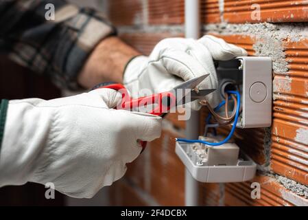 Un électricien au travail avec des ciseaux prépare les câbles électriques d'un système électrique résidentiel. Industrie de la construction. Banque D'Images