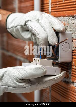 Un électricien au travail insère le câble électrique dans la pince d'un disjoncteur d'un système électrique résidentiel. Industrie de la construction. Banque D'Images