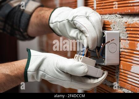 Un électricien au travail insère le câble électrique dans la pince d'un disjoncteur d'un système électrique résidentiel. Industrie de la construction. Banque D'Images