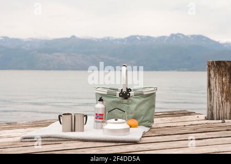 Panier pique-nique avec pommes, thermodurcissables et tasses en métal avec couverture sur le bois de la barbier. Pique-nique sur la mer en Norvège. Terre scandinave - randonnée en plein air. Banque D'Images