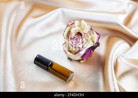 Divers contenants pour le stockage de cosmétiques en verre foncé se trouvent sur les plis de tissu satiné de soie, entouré de fleurs de rose séchées. Parfum, sérum ou Banque D'Images