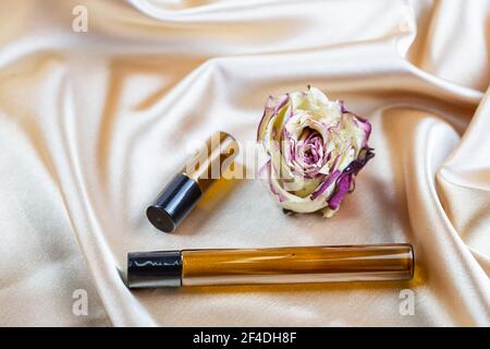 Divers contenants pour le stockage de cosmétiques en verre foncé se trouvent sur les plis de tissu satiné de soie, entouré de fleurs de rose séchées. Parfum parfum c Banque D'Images
