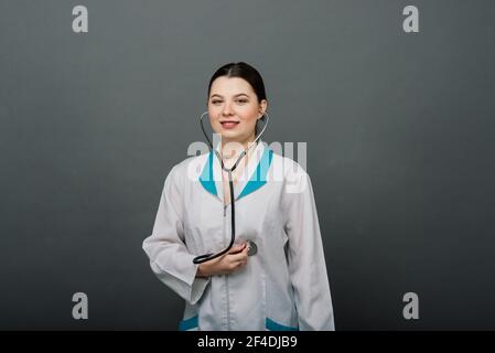 Belle femme médecin tenant stéthoscope souriant isolé sur fond gris. Banque D'Images