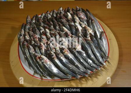 Les sardines de couleur argent frais sont disposées en rangées sur la plaque ronde en bois de la table. Banque D'Images