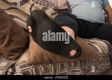 Un jeune homme avec une chaussette noire usée se relaxant sur un canapé.assis sur la toux. Banque D'Images