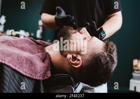 Rasage et soin de la barbe dans le salon de coiffure, l'application de gel cosmétique sur le cou et le visage du client masculin pour faire des hommes procédure de beauté. Banque D'Images