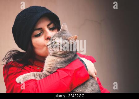 Une femme en rouge tenant et embrassant un chat tabby Banque D'Images