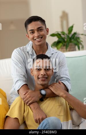 Portrait d'un couple gay masculin varié assis sur un canapé à l'appareil photo et souriant Banque D'Images