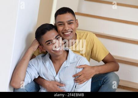 Portrait d'un couple gay masculin varié assis dans un escalier à l'appareil photo et souriant Banque D'Images
