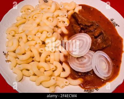 La goulash de cerf de Virginie avec des pâtes et des tranches d'oignon cru sur une assiette. Banque D'Images