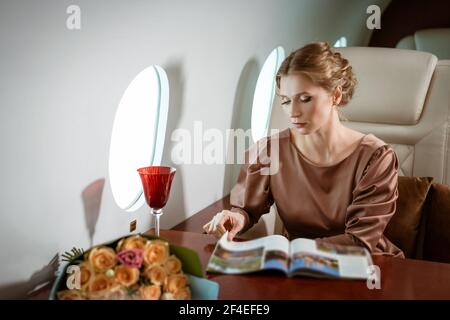 une jolie femme blonde habillée dans une élégante robe beige est présente dans un siège confortable sur un jet privé Banque D'Images