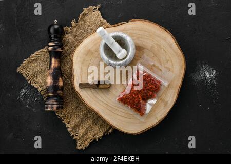 Section transversale en bois avec paprika écrasé dans un emballage en plastique et mortier et moulin à pierre Banque D'Images