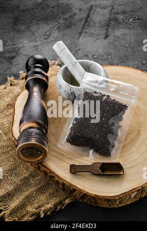 Section transversale en bois avec grains de poivre dans un emballage en plastique et pierre mortier et moulin Banque D'Images