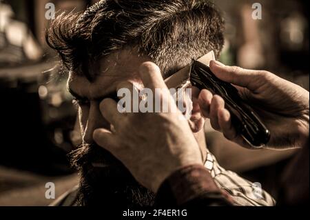 Le coiffeur fonctionne avec une tondeuse à cheveux. Client Hipster qui obtient une coupe de cheveux. Mains du coiffeur avec tondeuse cheveux, gros plan. Concept de coupe de cheveux. Homme visitant le coiffeur Banque D'Images