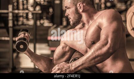 Bodybuilder s'entraîner avec des haltères à la salle de gym. Homme levant des haltères dans une salle de gym faisant de l'exercice pour les muscles. Homme bodybuilder faire des exercices Banque D'Images