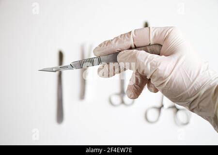 Une main de médecin avec un gant tenant un couteau chirurgical Banque D'Images