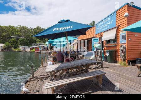 Les gens s'assoient sous de grands parasols à l'ombre de la chaleur Soleil d'été au café Tuross boatshed sur le New Pays de Galles du Sud côte sud en Australie Banque D'Images