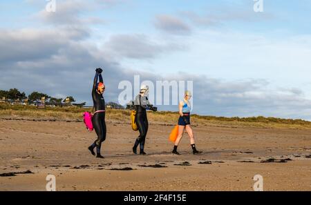 North Berwick, East Lothian, Écosse, Royaume-Uni, 21 mars 2021. Météo au Royaume-Uni : les nageurs sauvages nagent en eau libre dans le Firth of Forth. La natation sauvage est devenue un sport populaire pour les habitants de la ville balnéaire. Ces femmes sont quelques-uns des réguliers qui participent au sport chaque semaine tout au long de l'année. En photo : Sarah, JO et Alison nagent chaque semaine, parfois plus souvent à West Bay pendant qu'ils se préparent à aller dans la mer depuis la plage en portant des combinaisons et des flotteurs Banque D'Images