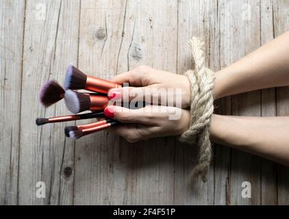 Les mains de la jeune femme avec les ongles rouges sont attachés et se trouvent sur fond de bois clair, elle tient des pinceaux de maquillage, concept sur la dépendance, la folie de beauté Banque D'Images