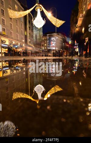 Vienne Graben rue à l'heure de Noël se reflète dans une flaque d'eau tandis que les touristes sont des visites et des magasins. Banque D'Images