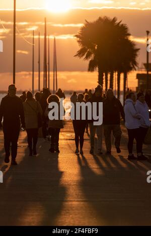 Personnes marchant sur la promenade du front de mer vers le coucher du soleil à Southend sur la mer, Essex, Royaume-Uni silhoueté par le soleil bas. Ombres longues et palmiers. Marche d'hiver Banque D'Images