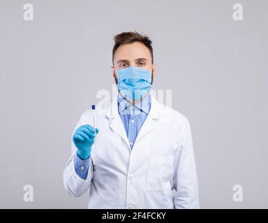 Médecin de sexe masculin dans un masque de protection et des gants portant un écouvillon stérile Bâton pour le test PCR du coronavirus sur fond gris Banque D'Images