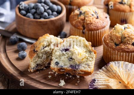 Muffin aux myrtilles coupé en deux avec beurre et baies et muffins en arrière-plan sur un plateau en bois Banque D'Images