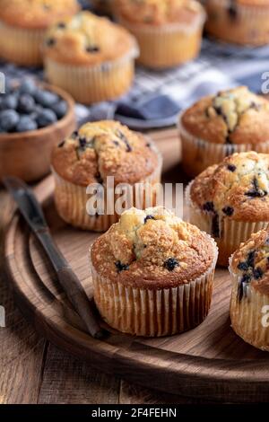 Muffins aux myrtilles sur un plateau en bois avec baies et muffins en arrière-plan Banque D'Images