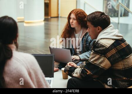 Groupe d'étudiants ayant une discussion sur les études au collège. Amis sur le campus universitaire avec ordinateur portable. Banque D'Images