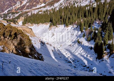 Le lit d'une rivière de montagne gelée parmi une épinette forêt avec maisons en arrière-plan en hiver Banque D'Images