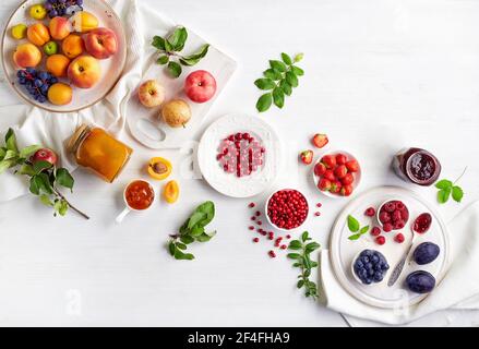 Composition à plat de confiture faite maison dans un pot en verre, fruits frais et baies sur une table en bois blanc Banque D'Images