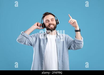 Un jeune homme insouciant écoute de la musique dans un casque bleu arrière-plan du studio Banque D'Images