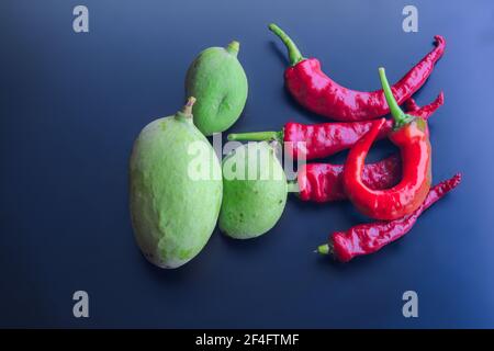 Vue de dessus des mangues vertes et des poivrons rouges sur fond sombre Banque D'Images