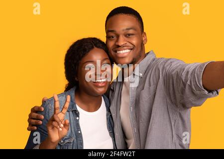 Joyeux jeune couple afro-américain qui prend Selfie sur fond jaune Banque D'Images
