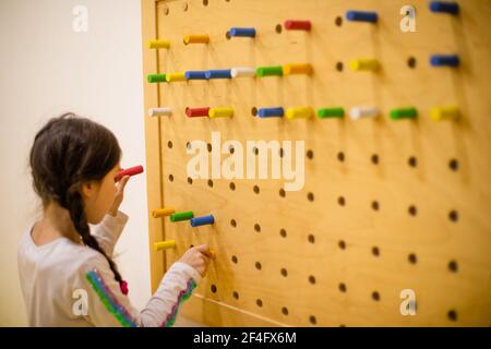 la fille joue avec des panneaux perforés en bois avec des chevilles rondes Banque D'Images