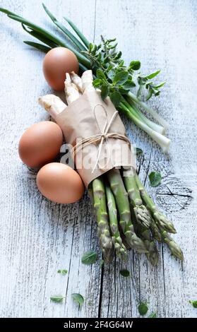 Groupe d'asperges crues avec œufs, oignons et herbes sur fond de bois. Directement au-dessus. Banque D'Images