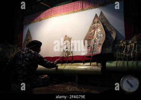 Le maître de marionnettes (dalang) interprète la représentation de wayang kulis « The Death of Kumbakarna » au Musée Sonobudoyo de Yogyakarta, dans le centre de Java, en Indonésie. Des figures allégoriques du Gunungan représentant à la fois l'arbre de vie javanais et la montagne Cosmique (Mont Meru) sont vues de chaque côté de l'écran. Le théâtre traditionnel de marionnettes connu sous le nom de wayang kulis est répandu sur les îles de Java et Bali en Indonésie. Chaque exécution de wayang kulit se poursuit environ huit heures par nuit sans intermissions et un seul maître de marionnettes (dalang) conduit toutes les marionnettes projetées sur un SC de lin Banque D'Images