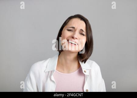 Expressions et émotions du visage humain. Portrait de la jeune femme multiethnique brunette en riant, en débardeur rose et en chemise blanche. Banque D'Images