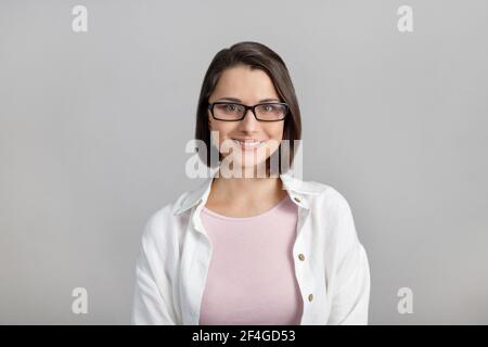 Portrait de race mixte, gaie, moderne, élégant, mignon, femme intelligente et souriante dans des lunettes sur fond gris, regardant l'appareil photo Banque D'Images