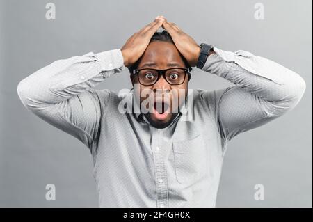 Portrait d'un jeune américain afro-américain fusé ou d'un employé portant une chemise à la recherche d'une expression choquée et coupable, tenant les mains sur sa tête, ouvrant la bouche largement, langage corporel, Oh non Banque D'Images