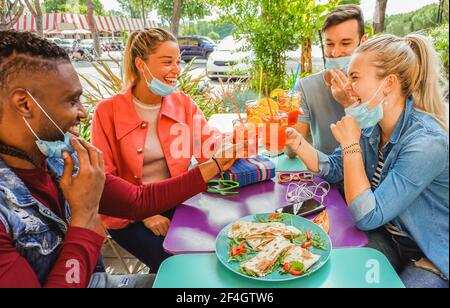 Amis qui boivent du coktail et qui mangent des tapas dans un bar du restaurant en plein air en été avec masque facial pour être protégé du coronavirus - heureux Banque D'Images