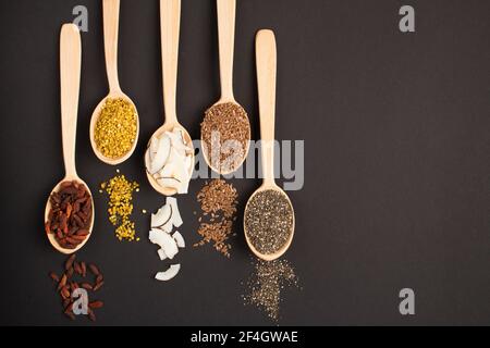 Vue de dessus de différents types de superaliments naturels dans le cuillères en bois sur fond noir Banque D'Images