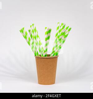 Pailles à boire en papier blanc et vert dans une tasse de papier jetable brune sur fond blanc. Le concept de l'abandon de la plaque. Banque D'Images