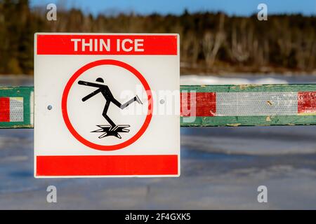 Un signe par un lac gelé avertissement de glace mince. Il est monté sur un vieux sawhorse vert qui possède également du ruban réfléchissant. Vue en gros plan. Banque D'Images