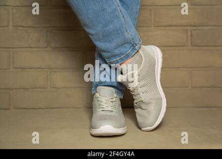 Chaussures de sport confortables pour femmes sur béton sur fond de mur de briques. Pied femme baskets jeans Banque D'Images