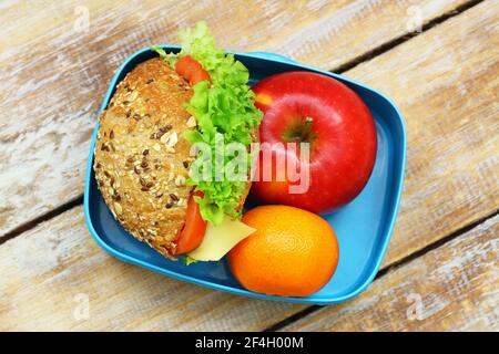 Boîte à lunch saine contenant un rouleau de fromage à grains entiers avec de la laitue et de la tomate, de la pomme et du satsuma Banque D'Images