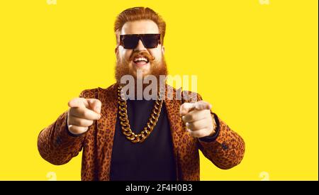 Homme dans la chaîne d'or et costume funky pointant les doigts vers caméra isolée sur fond couleur Banque D'Images