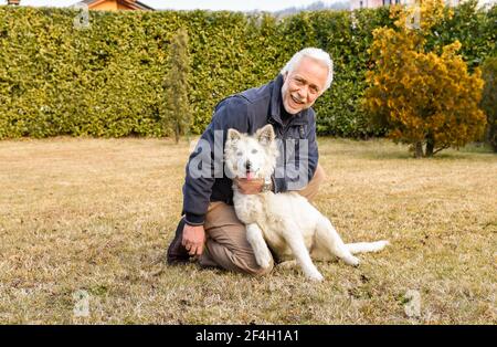 Homme senior jouant avec le chiot Berger blanc suisse dans le jardin. Banque D'Images